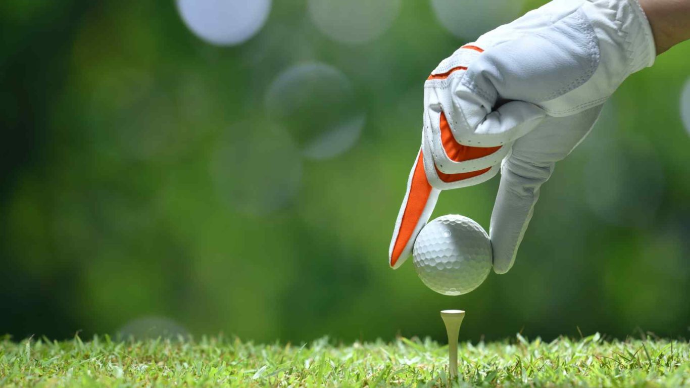 Person wearing golfing glove, placing a golf ball on a tee