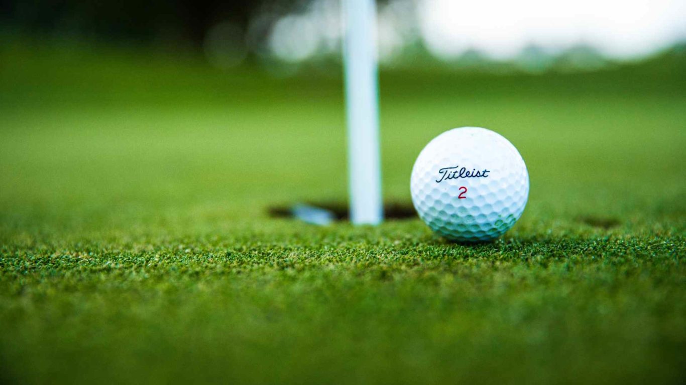close up of a Titleist golf ball next to golf hole