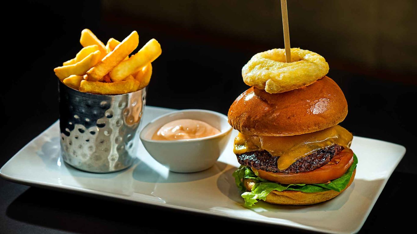 Image of beef burger with onion rings, chips and dip