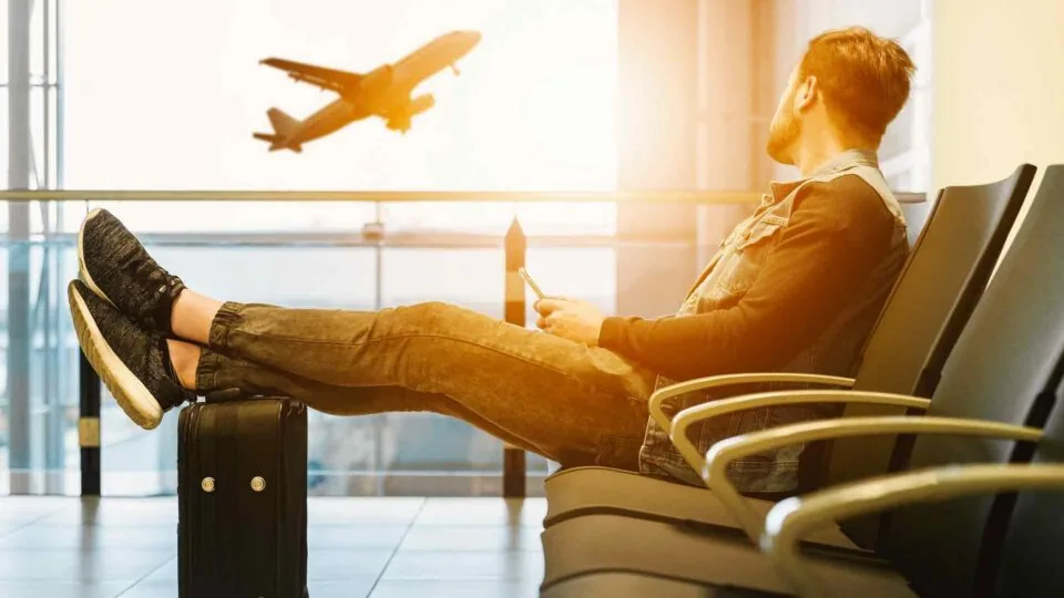 Man sitting in airport lounge with feet up on his suitcase watching an airplane take off. Shannon Springs Hotel is conveniently located near Shannon airport and has ample parking spaces, making it the best airport hotel with parking.